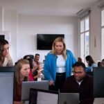 Employees in an office looking at some computers. Other employees sit at a table in the background.