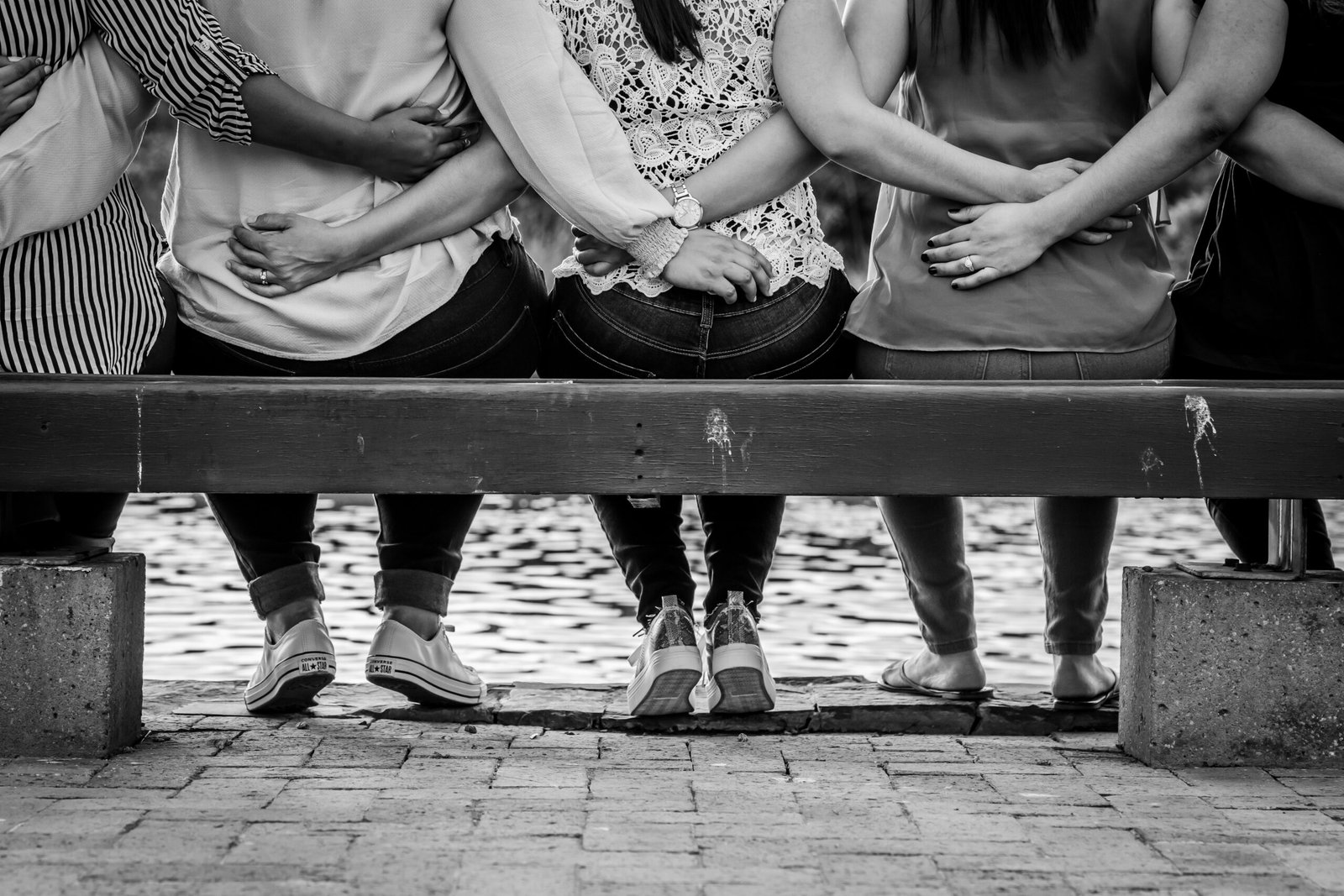 grayscale photo of 3 women sitting on wooden bench