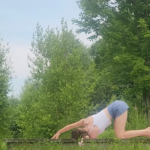 woman in thread the needle yoga pose on wooden platform outside in front of trees and horses