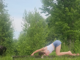 woman in thread the needle yoga pose on wooden platform outside in front of trees and horses