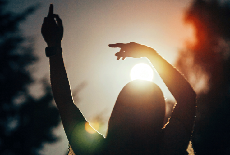 Silhouette of a woman standing outside as the Sun lowers as she contemplates her weekly horoscope for September 14-20, 2025