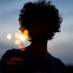 A silhouette of a woman at dusk holding a sparkler with the night sky behind her.