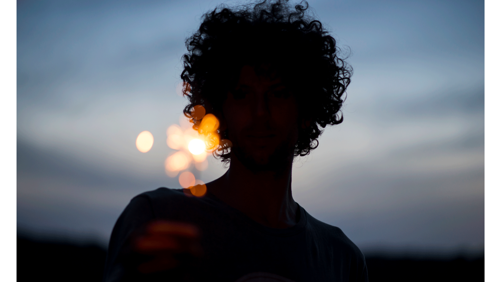 A silhouette of a woman at dusk holding a sparkler with the night sky behind her.