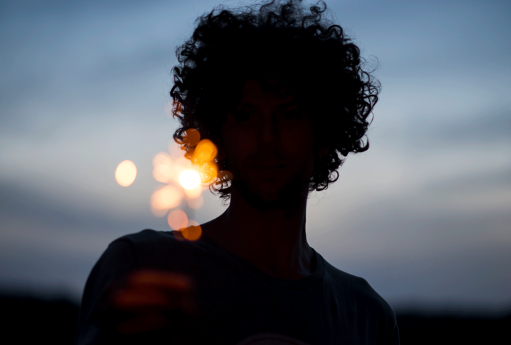 A silhouette of a woman at dusk holding a sparkler with the night sky behind her.