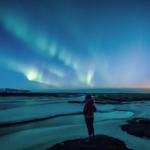 Woman standing beneath the northern lights on winter solstice contemlating weekly horoscope for December 21-27, 2025