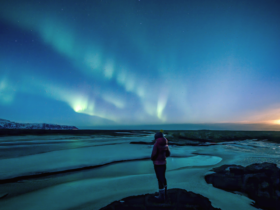 Woman standing beneath the northern lights on winter solstice contemlating weekly horoscope for December 21-27, 2025