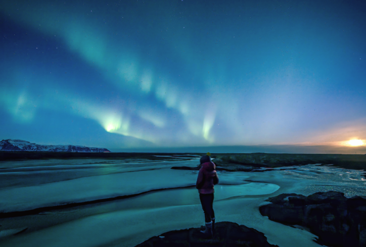 Woman standing beneath the northern lights on winter solstice contemlating weekly horoscope for December 21-27, 2025