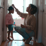 Mom measuring her toddler daughter during the childhood stage of life against a doorway