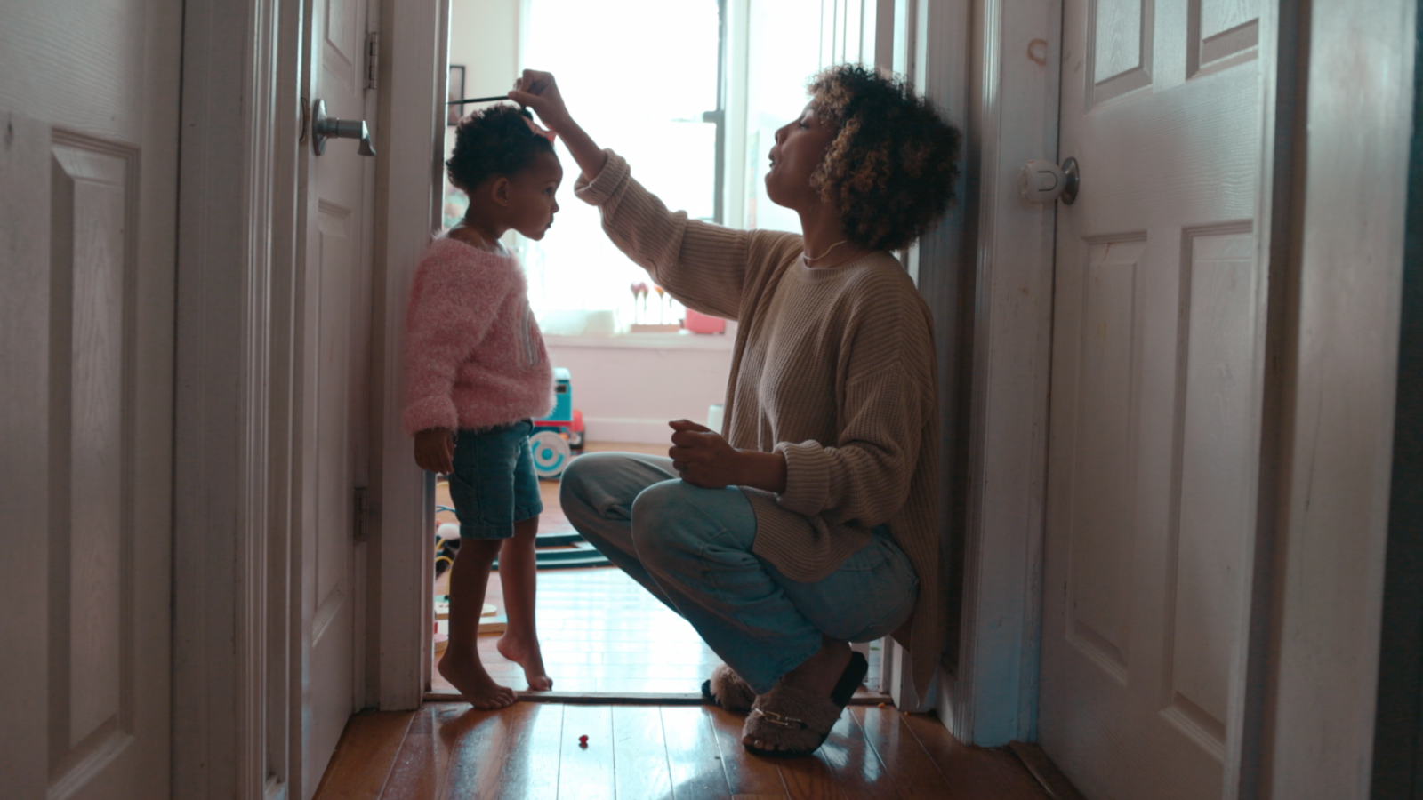 Mom measuring her toddler daughter during the childhood stage of life against a doorway