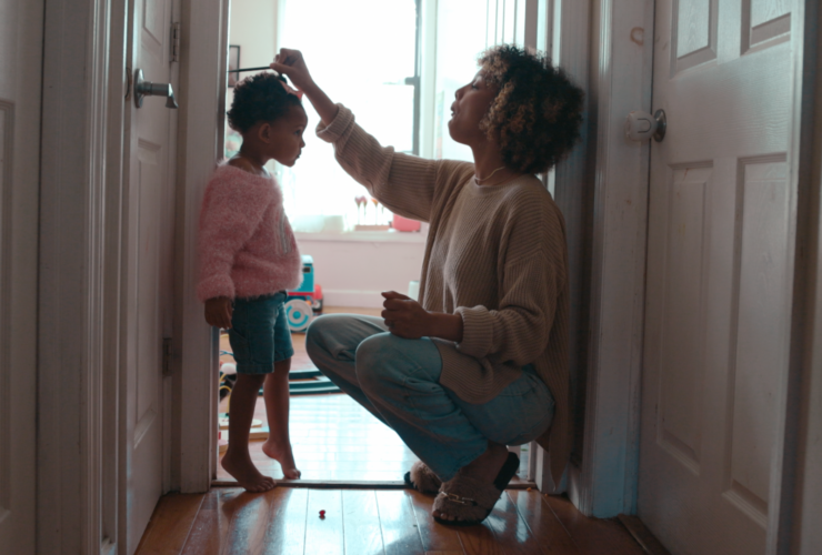Mom measuring her toddler daughter during the childhood stage of life against a doorway